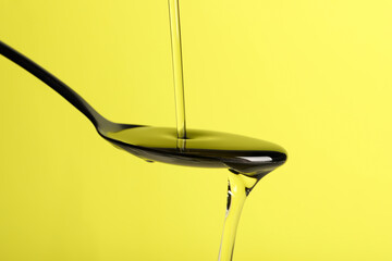 Pouring cooking oil into spoon on yellow background, closeup