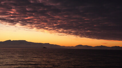 Popcorn clouds illuminated pink over the silhouette of a mountain, at sunset at Cierva Cove, Antarctica
