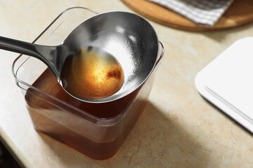 Container and ladle with used cooking oil on beige table