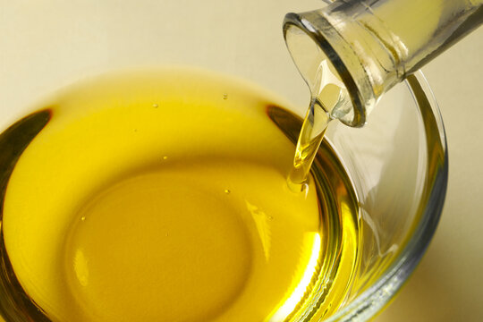 Pouring cooking oil from bottle into bowl on white background, closeup