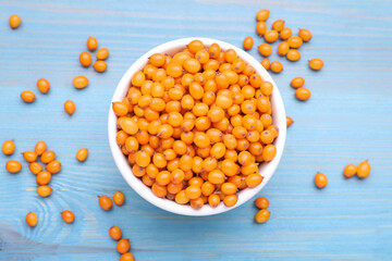 Bowl with fresh ripe sea buckthorn berries on light blue wooden table, flat lay