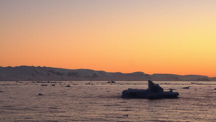 Sunset silhouetting icebergs floating in the Southern Ocean, at Cierva Cove, Antarctica