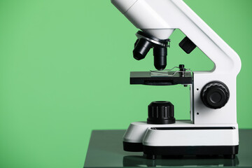 Modern medical microscope on table against green background, closeup. Space for text