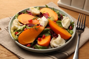 Delicious persimmon salad with cheese and pomegranate served on wooden table