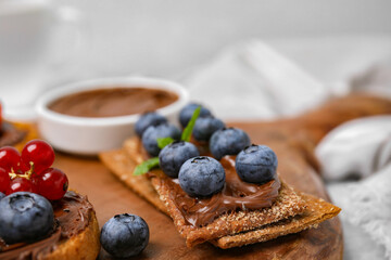 Fresh crunchy rye crispbreads with chocolate spread and blueberries on wooden board, closeup
