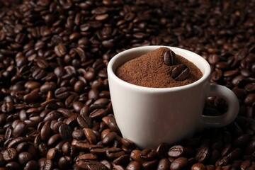 Cup with ground coffee on roasted beans. Space for text