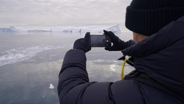 Man filming on smart phone icebergs at sea