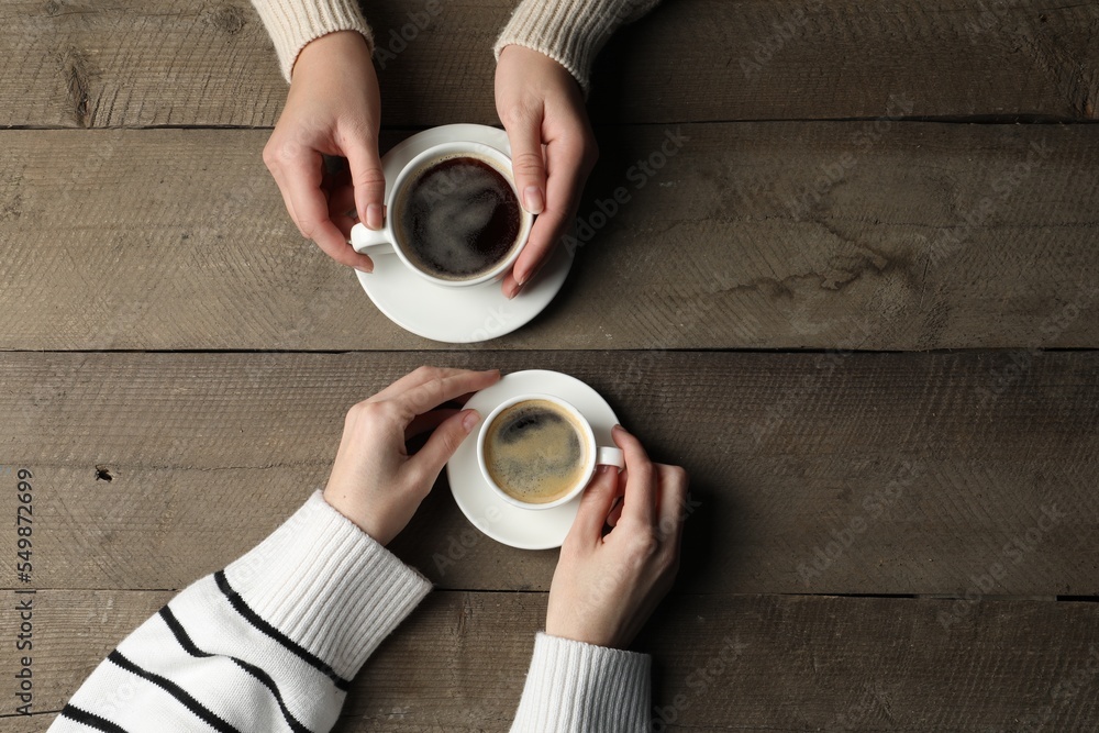 Canvas Prints Women with cups of aromatic coffee at wooden table, top view. Space for text