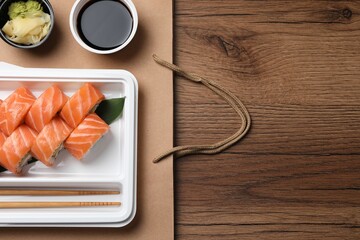 Food delivery. Delicious sushi rolls served on wooden table, flat lay with space for text