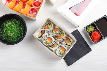 Food delivery. Paper boxes with delicious sushi rolls on white wooden table
