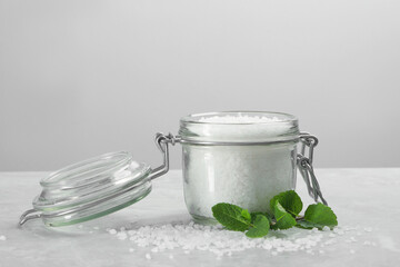 Natural sea salt in glass jar and mint on light grey marble table