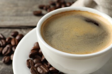 Cup of hot aromatic coffee and roasted beans on wooden table, closeup. Space for text