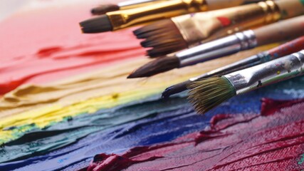 Fototapeta premium Many brushes on artist's palette with colorful mixed paints, closeup