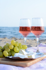 Glasses with rose wine and snacks for beach picnic on sandy seashore