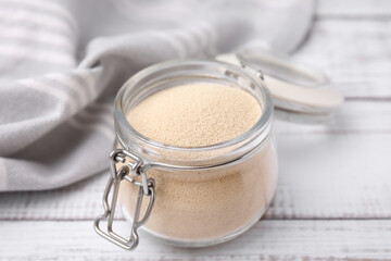 Granulated yeast in glass jar on white wooden table, closeup