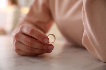Woman holding wedding ring at table indoors, closeup. Divorce concept - obrazy, fototapety, plakaty