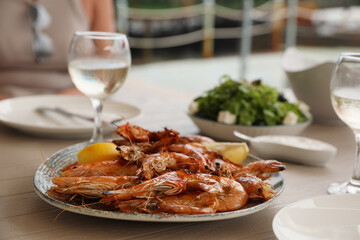 Plate of delicious cooked shrimps served with lemon and wine at table outdoors, closeup
