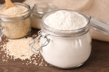 Jars with quinoa flour and seeds on wooden table, closeup