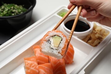 Woman eating sushi rolls with chopsticks at white table, closeup