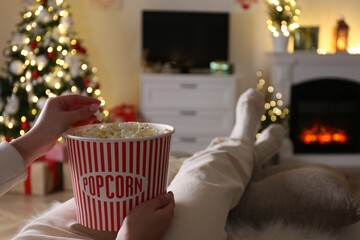 Woman with popcorn watching TV in room decorated for Christmas, closeup