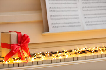 Gift box and fairy lights on piano keys, closeup. Christmas music
