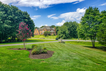 Obraz premium large, luxurious, brick house with landscaping and a huge green lawn. Landscape on a summer sunny day under a blue cloudy sky.