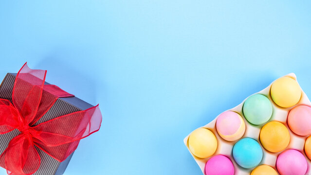 Easter pastel background with colorful eggs and a gift box with red bow on a blue background. The concept of a Happy Easter. Top view, copy space.