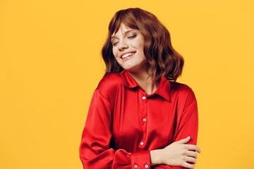 a pleasant, charming woman stands in a stylish red shirt on a yellow background and smiles sweetly with her eyes closed. Horizontal photo with an empty space for inserting an advertising layout