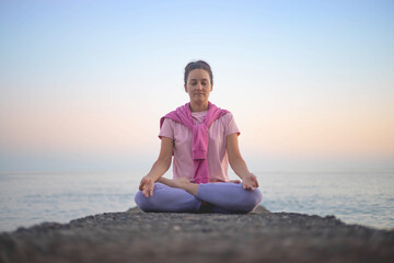 Naklejka na ściany i meble Yoga woman meditation in lotus position at pebble sea beach sunset sky horizon healthy lifestyle
