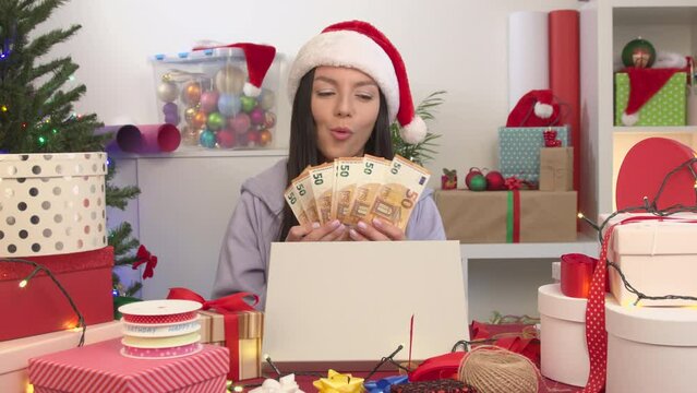 Euro banknotes Money in cash as a Christmas gift. Happy young woman in a Santa hat showing a cash mone. A lot of gift cardboard box on christmas background