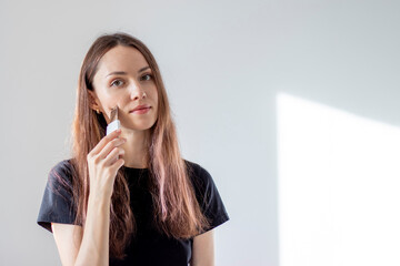 Young woman cleanses her facial pores with an ultrasonic scrubber. Self-care at home. Girl wants...