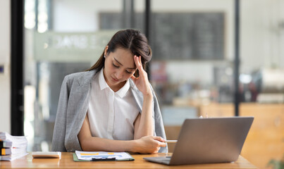 Fototapeta premium Portrait of tired young business Asian woman work with documents tax laptop computer in office. Sad, unhappy, Worried, Depression, or employee life stress concept