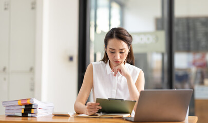 Portrait of tired young business Asian woman work with documents tax laptop computer in office. Sad, unhappy, Worried, Depression, or employee life stress concept