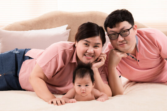 Happy asian family laying down and taking pictures together in bedroom. parents and little daughter looking at camera posing for photo. Exemplary family portrait, love and bond concept