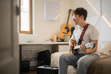 Young man playing electric guitar singing song sitting on bed at home enjoy audio sound