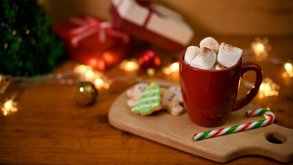 A cup of hot chocolate with marshmallow on wooden table with Christmas decor.