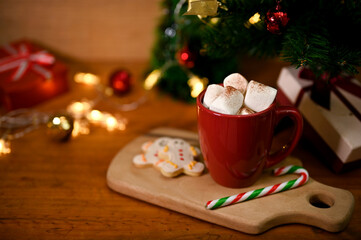 Obraz na płótnie Canvas A cup of hot chocolate with marshmallow, gingerbread and candy on wood board on wooden table