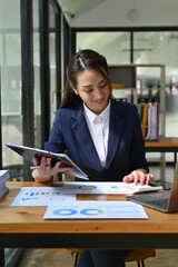 Charming Asian businesswoman working at her desk, using calculator, calculating sales and profit