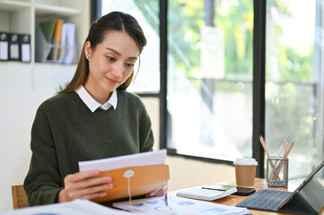 Beautiful Asian businesswoman opening the letter or document for reading, working at her desk.