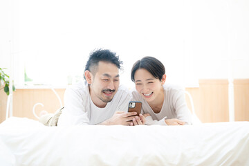 Fototapeta premium Image of an Asian couple lying down and looking for something on their phone. 