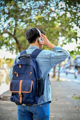 Asian male traveler listening to music though his headphones while strolling around the city. back...