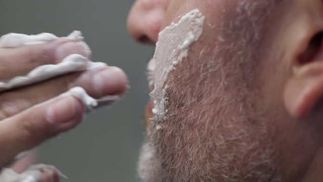 Close-up shot of unrecognized male chin while shaving. Detailed view of a barber covering cheekbones with a thick, white shaving foam. High quality 4k footage