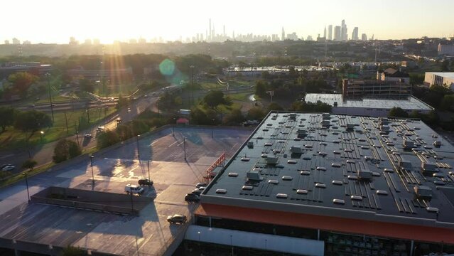 Aerial dolly in over industrial buildings with solar panels at sunrise, with New York cityscape in the distance