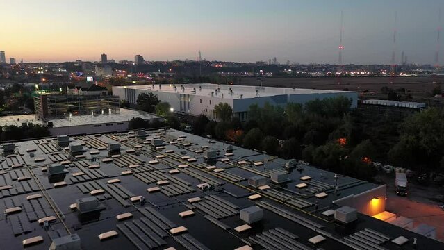 Aerial dolly in over industrial buildings with solar roof panels and cityscape in the distance