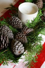 christmas composition with a candle, pine cones and green needles with red table runner 