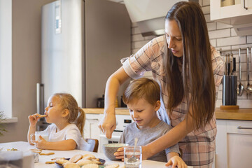 Mom and children prepare icing for gingerbread in their home kitchen. Beat with a blender. The girl...