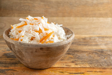 Sauerkraut in wooden bowl over rustic background.