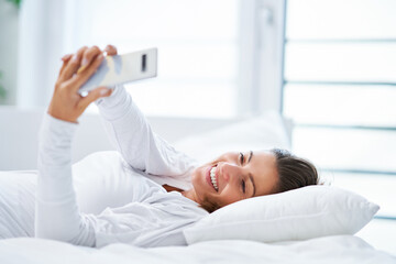 Young brunet woman with smartphone on the bed