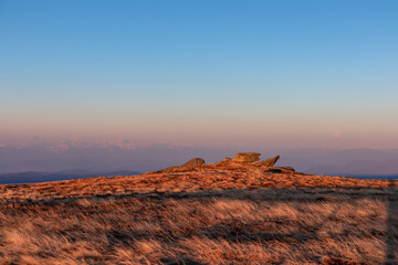 Scenic view of rock formation and Karawanks mountains at sunrise seen from alpine meadow at Ladinger Spitz, Saualpe, Lavanttal Alps, Carinthia, Austria, Europe. Early morning golden hour in Wolfsberg