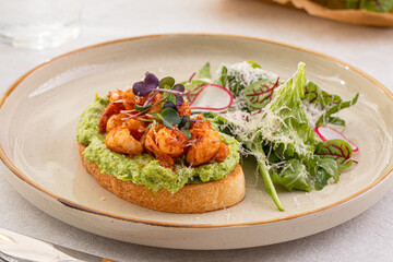 Portion of avocado toast with grilled shrimp and salad